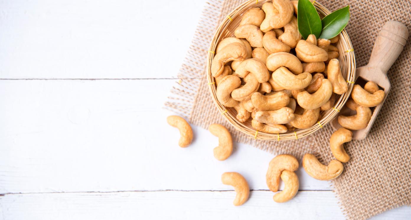 Cashew nuts with green leaves in basket and spoon isolated on white wooden background, selective focus, Healthy food