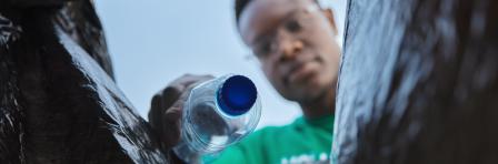 Recycle, bottle and black man with view in bag, sustainability and cleaning plastic pollution, earth day and community service. Saving the environment, charity and people putting trash in garbage bin